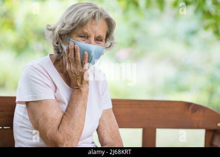 Donna anziana che indossa una maschera protettiva contro il virus corona Foto Stock