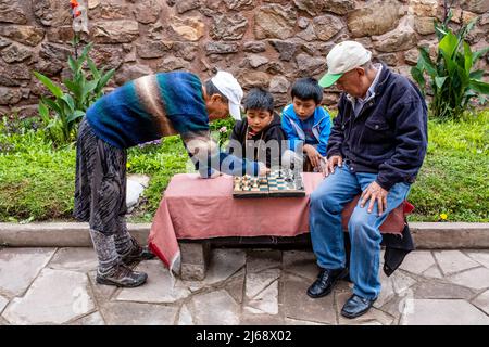 Due uomini che giocano a Scacchi guardati da bambini locali, Pisac, la Valle Sacra, Provincia di Calca, Perù. Foto Stock