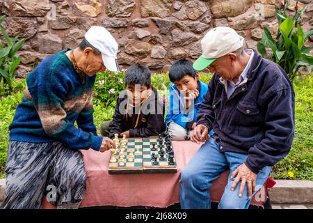 Due uomini che giocano a Scacchi guardati da bambini locali, Pisac, la Valle Sacra, Provincia di Calca, Perù. Foto Stock