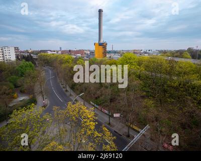 Paesaggio della città durante il tramonto. Centrale elettrica dell'impianto di cogenerazione di fronte allo skyline. Alberi verdi e una strada in primo piano. Foto Stock