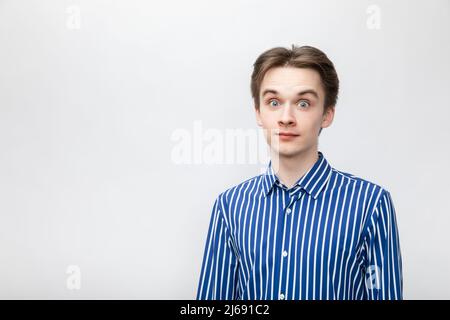 Ritratto di stupito stupito giovane uomo con camicia a bottoni blu-bianco a righe con occhi aperti. Studio girato su sfondo grigio Foto Stock