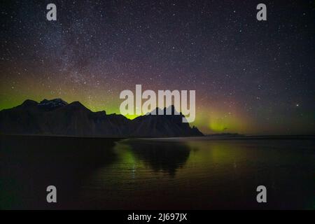 Aurora boreale (Aurora Borealis) e Via Lattea sopra il monte Vestrahorn, riflettendo in acqua, penisola di Stokksnes, Islanda sudorientale, regioni polari Foto Stock