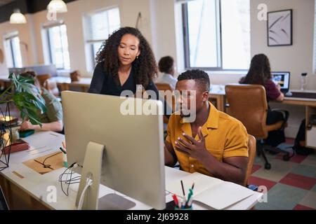 Una scena d'ufficio con due colleghi in discussione mentre guardano uno schermo Foto Stock