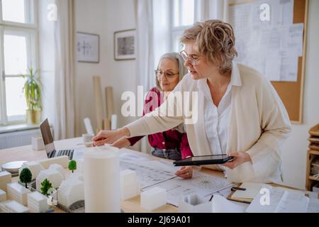 Le donne mature eco architetti con modello di moderni bulidings e progetti che lavorano insieme in ufficio. Foto Stock