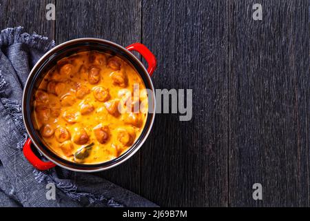 nakkikastike, salsicce finlandesi, amalgami in salsa di pomodoro cremosa in pentola rossa su tavola di legno scuro, vista orizzontale dall'alto, posa piatta, spazio libero, primo piano Foto Stock