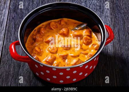 nakkikastike, salsicce finlandesi, amalgami in salsa di pomodoro cremosa in pentola rossa su tavola di legno scuro, vista orizzontale dall'alto, primo piano Foto Stock