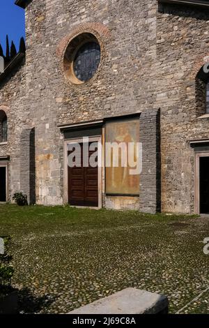 Austera facciata medievale della chiesa è impreziosita da un sbiadito affresco lombardo del 1300s di San Cristoforo, che indossa un abito rivestito di pelliccia, che porta il Cristo Bambino sulla spalla. La Chiesa di San Giorgio, fondata nel 1250 e consacrata nel 1313, a Varenna, sulla sponda orientale del Lago di Como, Lombardia, Italia. Foto Stock