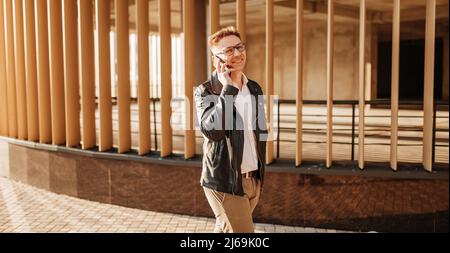 Bell'uomo con occhiali con uno smartphone sulla strada di una grande città. Uomo d'affari che parla al telefono su sfondo urbano Foto Stock