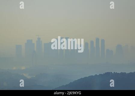 Vista in lontananza di alte sagome degli edifici in lontananza sotto la fitta nebbia al mattino Foto Stock