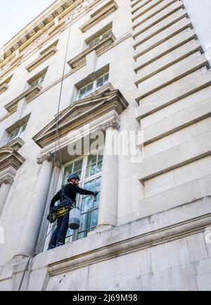 Abbeiling pulitore di finestra al lavoro su un elegante edificio di Londra Foto Stock