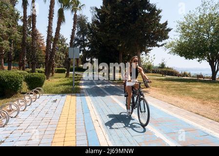 Madre e bambino attivi che cavalcano una bicicletta insieme su sfondo all'aperto. Donna caucasica e bambino su una bicicletta Foto Stock
