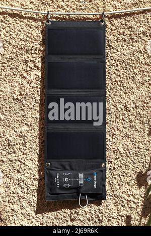 Un pannello solare che carica un dispositivo elettronico. Contro un muro e sole pieno Foto Stock