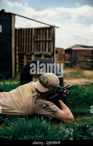 Soldato che si trova sull'erba mentre si punta una pistola in una partita Airsoft Foto Stock