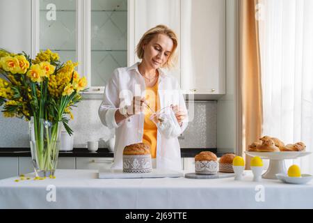 Una donna in cucina decora i dolci pasquali. Foto Stock