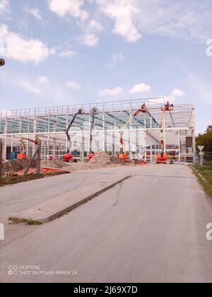 Un moderno edificio per uffici in costruzione con un pilone elettrico in primo piano Foto Stock