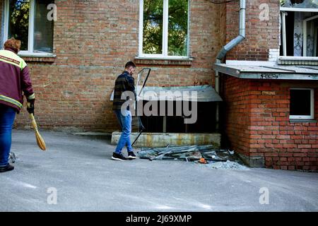 Un residente raccoglie le finestre di vetro rotte da un edificio residenziale dopo essere stato danneggiato dall'attacco russo di sgranatura a Kiev. I missili hanno colpito edifici residenziali nel centro di Kiev quando la Russia ha invaso l'Ucraina il 24 febbraio 2022, innescando il più grande attacco militare in Europa dalla seconda guerra mondiale Foto Stock