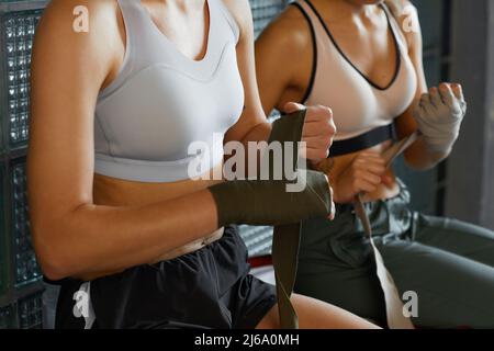 Due donne sportive irriconoscibili che avvolgono le mani con bende elastiche prima di sparring partita Foto Stock