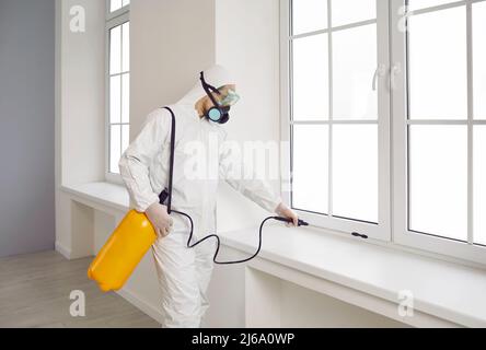 Operatore per il controllo delle peste in tuta protettiva e maschera spray chimico sopra la finestra della casa Foto Stock