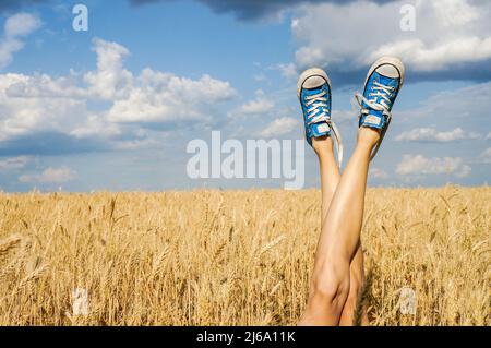 le gambe femminili indossano sneakers sul campo e sul cielo nuvoloso Foto Stock