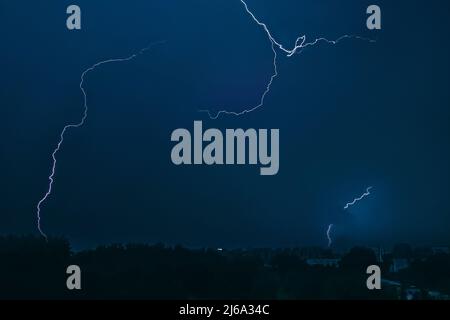 Fulmine nel cielo sopra la città. Luce lampeggiante nelle ore notturne scure. Thundernubi e scariche elettriche nell'atmosfera. Paesaggio urbano notturno. Foto Stock