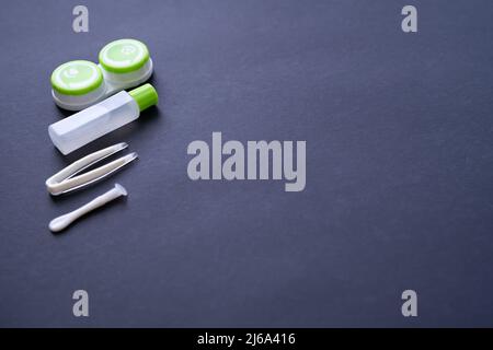 Contenitore con lenti a contatto, pinzette, ventosa e bottiglia con soluzione su sfondo blu, vista dall'alto, spazio di copia Foto Stock