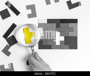 Mano con lente d'ingrandimento sopra il pezzo eccellente adatto del puzzle. Pensiero logico, concetto di analisi di situazione. Importante aggiunta di elementi mancanti. Unicità, concetto di individualità. Foto di alta qualità Foto Stock
