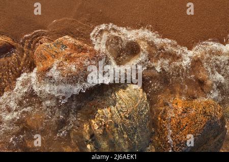 Direttamente sopra Shot di piccole onde che rotolano in spiaggia formando una forma del cuore nell'acqua schiumosa Foto Stock