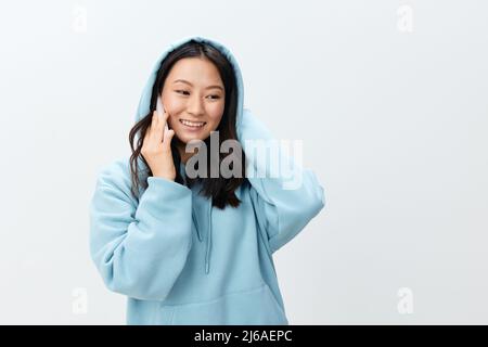 Bella felice Coreano giovane femmina in blu Hoodie tenere telefono parla con il ragazzo posa isolato su sfondo bianco studio. La migliore offerta Foto Stock