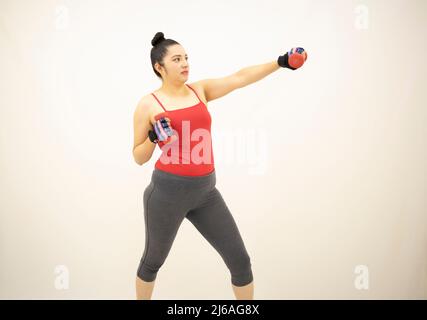 donna atletica carina che indossa abbigliamento sportivo grigio, top rosso, pratica boxe, manubri, lanciare pugni in avanti con braccio sinistro, su sfondo bianco Foto Stock
