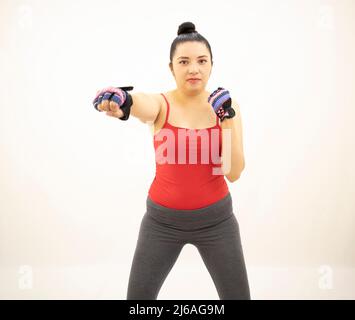 donna atletica asiatica che indossa una blusa rossa grigia da abbigliamento sportivo, allenando la punzonatura, praticando la boxe, sfondo bianco Foto Stock