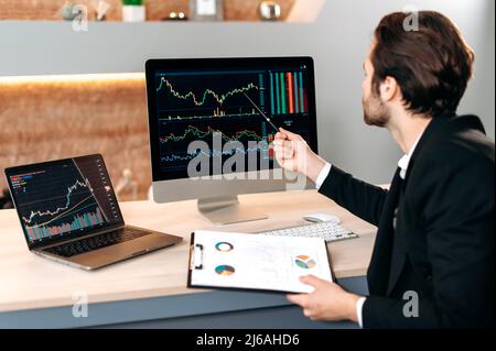 Un investitore di successo del commerciante maschio caucasico, che analizza il mercato finanziario di criptovaluta, guarda al calcolatore, che si occupa di una strategia di criptovaluta, che analizza i rischi. Investimenti, negoziazione in borsa Foto Stock