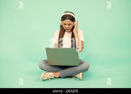 scioccato bambino ragazza influencer utilizzare il computer per videochiamata o ascoltare webinar in cuffia, blogging. Foto Stock
