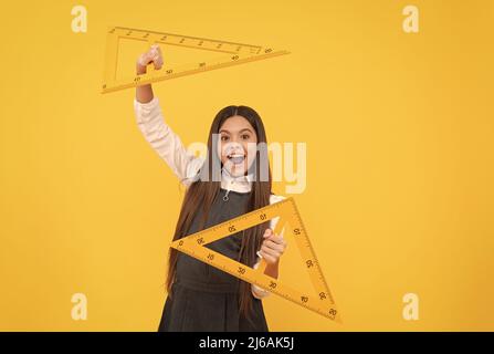 felice capretto tiene il righello di triangolo di matematica nella scuola su sfondo giallo, l'istruzione Foto Stock