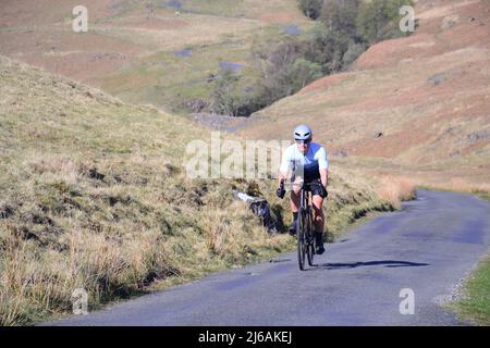 Cumbria, Regno Unito, 29th aprile 2022. Un ciclista maschio scorre verso il Passo di Hardknott. Sole caldo nella valle di Duddon, il Lake District, Cumbria, Regno Unito, come il fine settimana di festa della Banca comincia. Credit: Terry Waller/Alamy Live News Foto Stock
