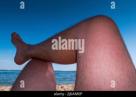 Le gambe dell'uomo stanno prendendo il sole su una spiaggia. Punto di vista. Foto Stock