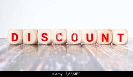 Cubetti di legno con la parola SCONTO stand su uno sfondo di legno tra una lente d'ingrandimento e una penna Foto Stock