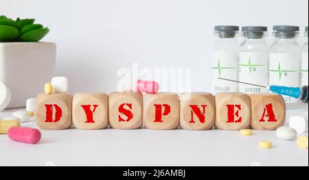La parola DISPNEA è scritta su cubi di legno vicino ad uno stetoscopio su sfondo di legno. Concetto medico. Foto Stock