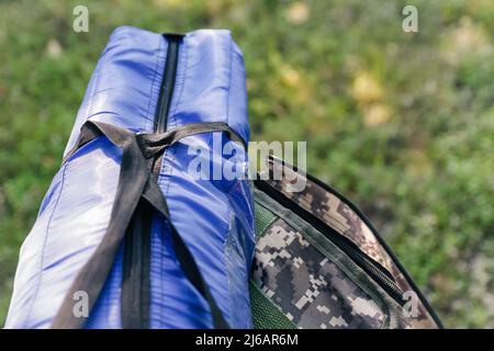 Zaino militare defocus e tenda blu o sacco a pelo. Borsa esercito su sfondo verde erba vicino albero. Zaino militare mimetizzazione. Turismo summ Foto Stock