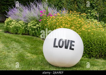 Grande palla gonfiabile bianca con L'AMORE stampato su di esso all'interno di uno sfondo colorato Foto Stock