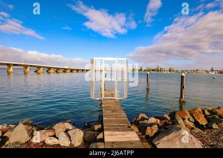 Cancello di sicurezza sul piccolo molo per ormeggio barca nel lago Wallis con ponte Forster-Tuncurry in background in giorno limpido Foto Stock