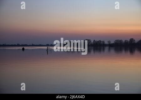 Canoe e una barca su un lago nella campagna italiana al tramonto Foto Stock