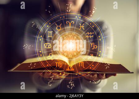 Donna che tiene un libro di astrologia. Proiezione ruota astrologica, scegliere un segno zodiacale. Astrologia concetto esoterico. Foto Stock