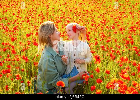 Buona famiglia primaverile. Famiglia felice che riposa su un campo di papavero bello. Divertimento all'aperto per tutta la famiglia. Madre e figlia stanno giocando nel campo di Foto Stock