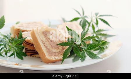 Rotolo dolce con olio di marijuana su piatto bianco. Cucina di cannabis. Disposizione dei deliziosi dessert, vista dall'alto da vicino. Foto Stock