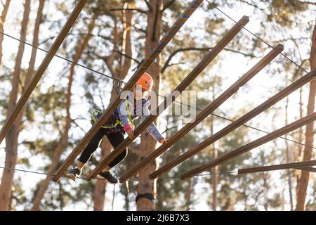 La bambina è in piedi su una corda, tenendo una corda con le mani. Un bambino in un parco funi supera gli ostacoli Foto Stock