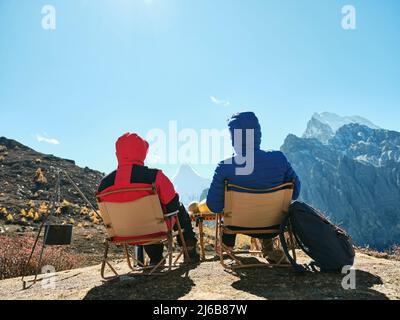 vista posteriore della coppia asiatica seduta in sedie sulla cima della montagna guardando la vista nel parco nazionale yading, contea di daocheng, provincia di sichuan, cina Foto Stock