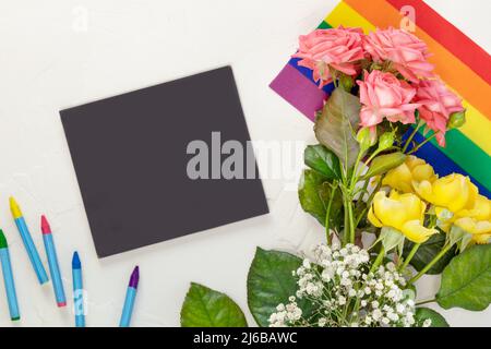 Composizione LGBT con rose rosa e giallo su bandiera arcobaleno e lavagna con gessi su sfondo bianco. 17 maggio, Giornata Internazionale contro Homo Foto Stock