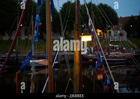 Carolinensiel, Germania - 14 agosto 2021: Vecchia lampada da strada su un palo di legno e vecchie barche a vela in legno durante l'evento Wattensail 2021. Foto Stock