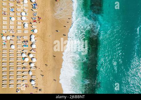 riprese aeree da un drone su una spiaggia di sabbia con persone che prendono il sole e rilassarsi. Vista piatta della costa e delle onde turchesi del surf e della gente Foto Stock