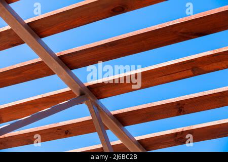 Le travi in legno del tetto si appoggiano su un telaio di acciaio, la struttura moderna è sotto il cielo blu profondo in una giornata estiva soleggiata Foto Stock